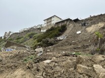 Portions of a home have broken off and slid down a hill. The sky looks gray and stormy.