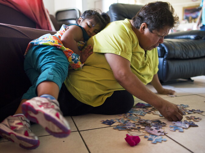 Three-year-old Soledad Garcia lays on her grandmother's back as they put a "Frozen" puzzle together on Monday afternoon, August 3, 2015.