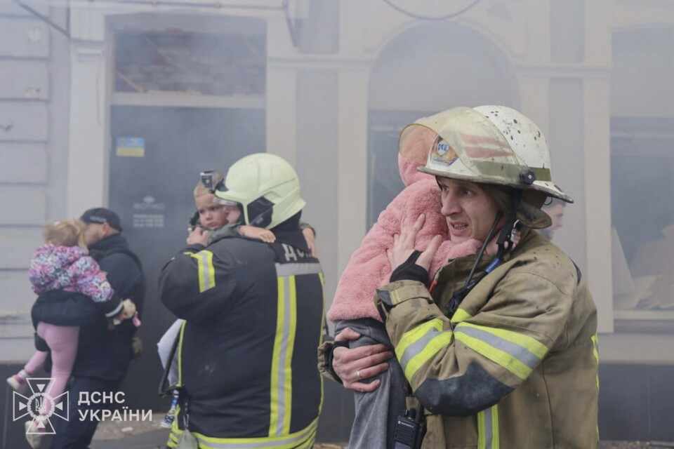 
People in firefighting gear carry children from a smoke-filled building.