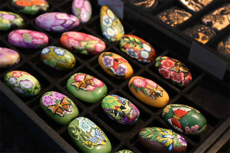 More than a dozen polished rocks/beads — mostly green with floral designs — sit in a tray.