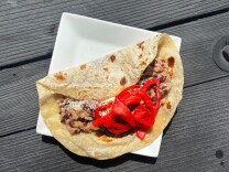 A Honduran baleada on a white plate, filled with mashed beans, sprinkled cheese, and topped with bright pickled red onions, all wrapped in a warm flour tortilla.