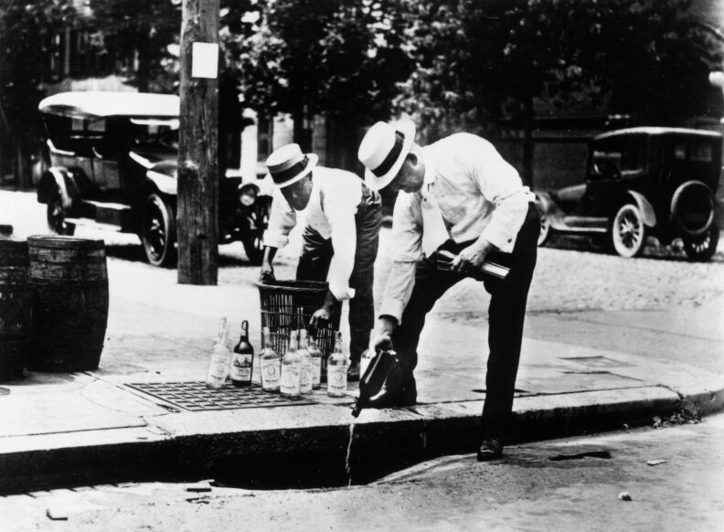 circa 1920: Two men pouring alcohol down a drain during prohibition in America.