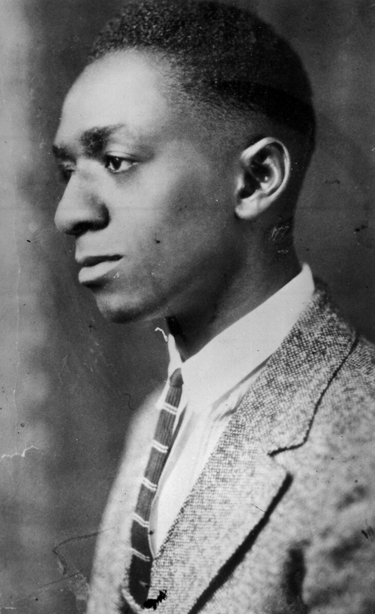 a headshot of a young black mean wearing a suit and tie. he looks seriously off into the distance