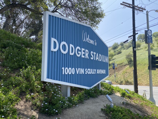 A sign with white lettering on a blue background reads, Welcome to Dodger Stadium, 1000 Vin Scully Avenue.