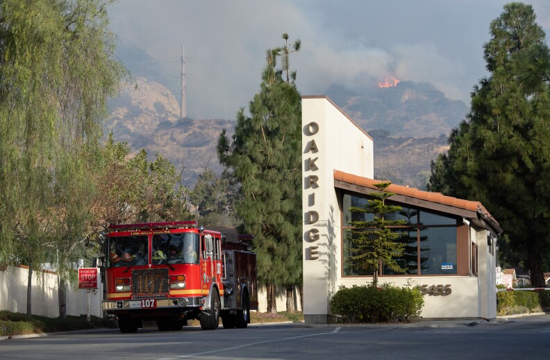 A fire truck exits a residential area with a sign that reads "Oakridge." A fire can be seen burning in the background.