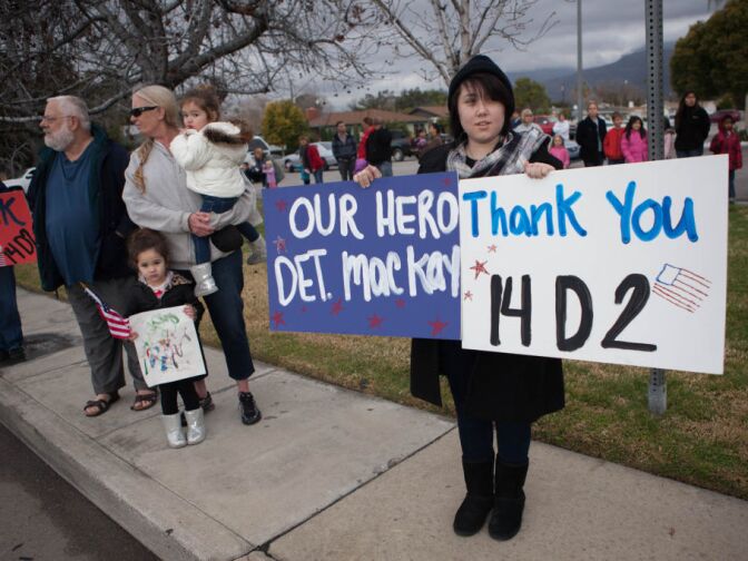 Jeanie Orillo holds signs thanking Det. Jeremiah MacKay as a long funeral procession passes by.