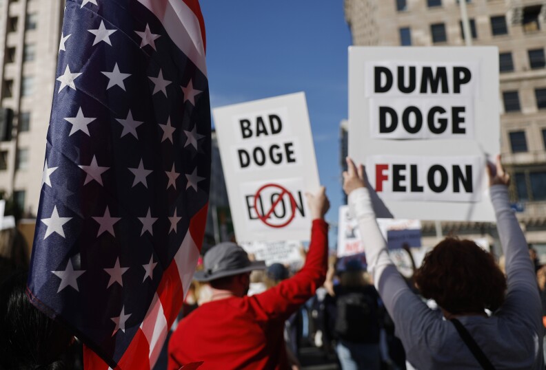 Protesters old up anti Elon Musk signs. A U.S. flag is in the foreground.