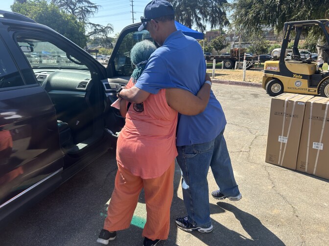 Two people hug each other in a parking lot under the sun. 