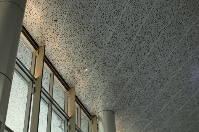 A close-up of the ceiling made up of square tiles with black dots on them next to a large window with silver framing.