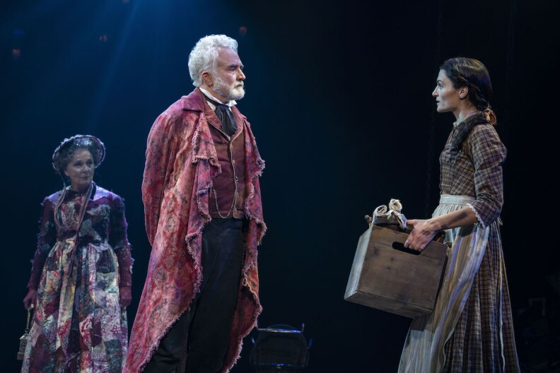 a woman in a brown Victorian dress holds a wooden box and talks to a man in an expensive red vest and robe