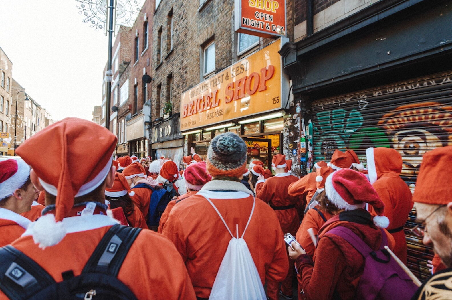 A crowd of people dressed as Santa Claus gather outside a bagel shop.