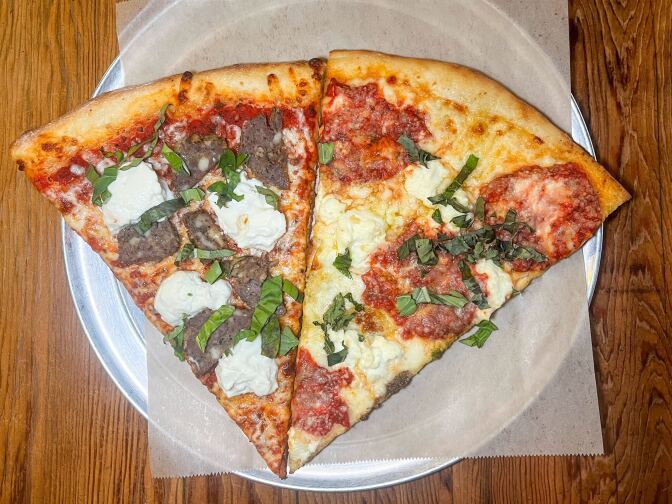 On a round metal tray, there are two slices of pizza. The slice on the left has meatballs with large dollops of white cheese and cut pieces of green basil on a lightly toasted pizza crust. The slice on the right has melted white cheese with large portions of red sauce and more cut pieces of green basil.