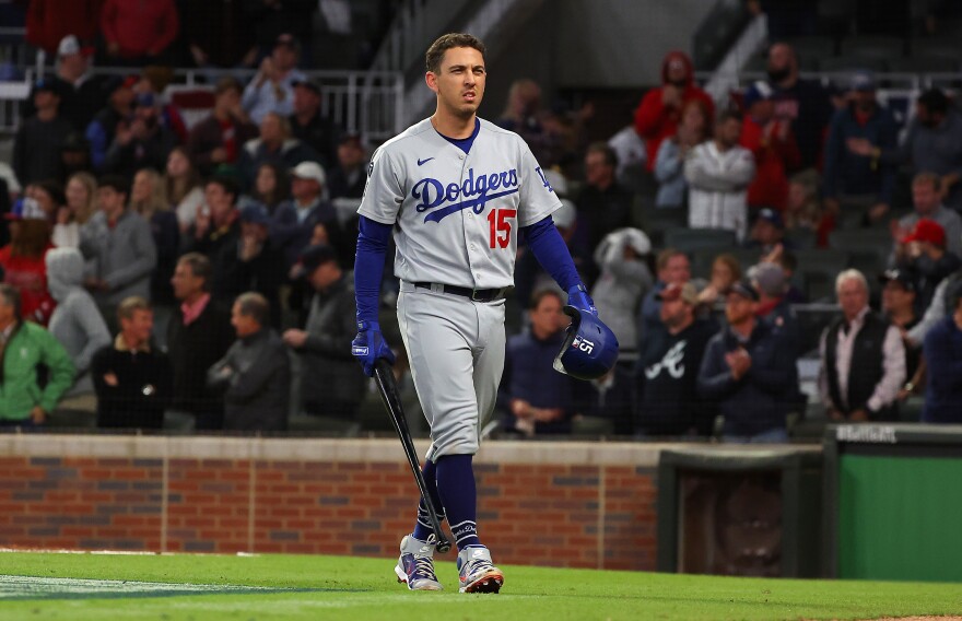Austin Barnes, number 15 of the Los Angeles Dodgers, is shown walking off the field while holding a bat. He wears a Dodgers uniform.