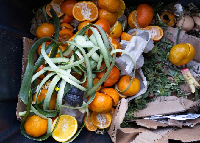 A black tote full of food waste, including cucumbers, citrus and strawberry tops.