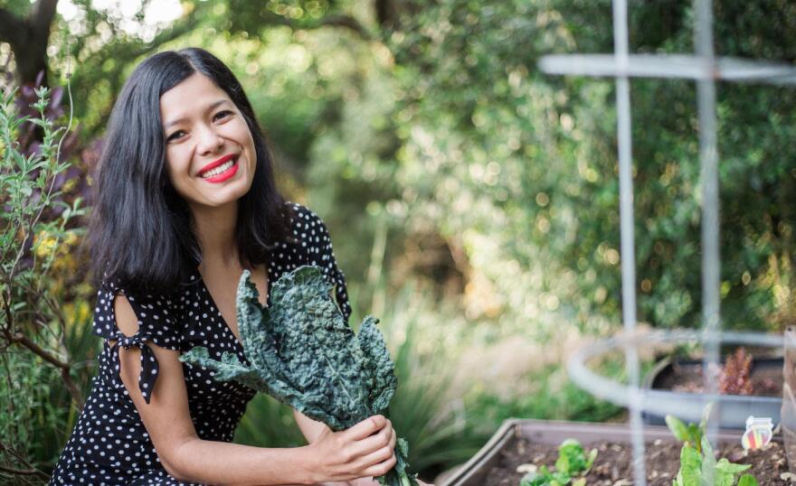 A woman with long dark hair smiles as she holds a leafy green plant.