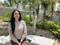 A young woman with long dark hair sits in a garden surrounded by blue ribbons.