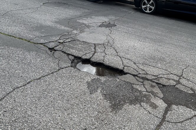 A close up of a street with a cracked pothole in the middle, which is full of rain water.