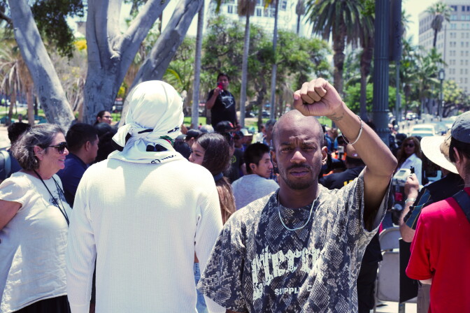 A man holds his fist in the air in front of a crowd of protesters.