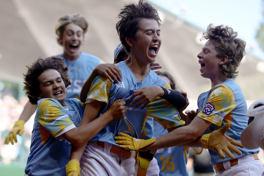 A group of preteen Little League baseball players are jumping around in celebration.