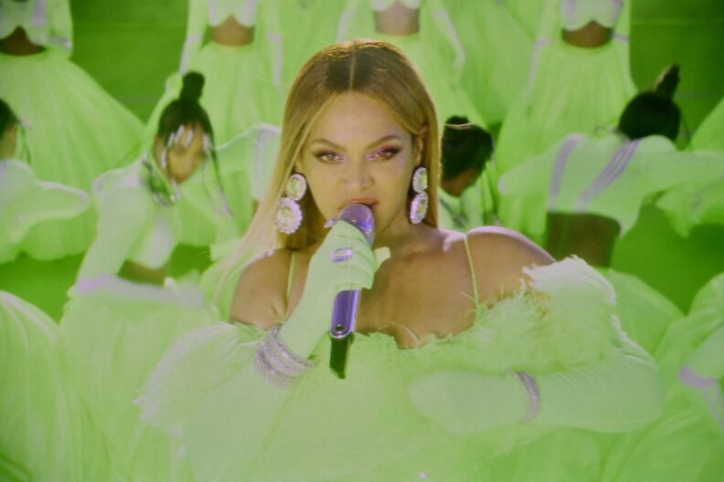Beyoncé performs in a lime green dress and large earrings, behind her other performers are in the same color.