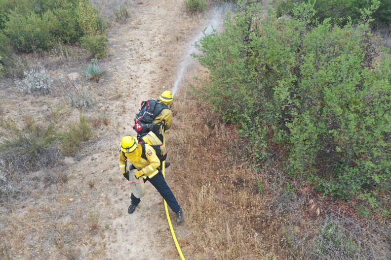 Two firefighters spraying water on dry vegetation during training.