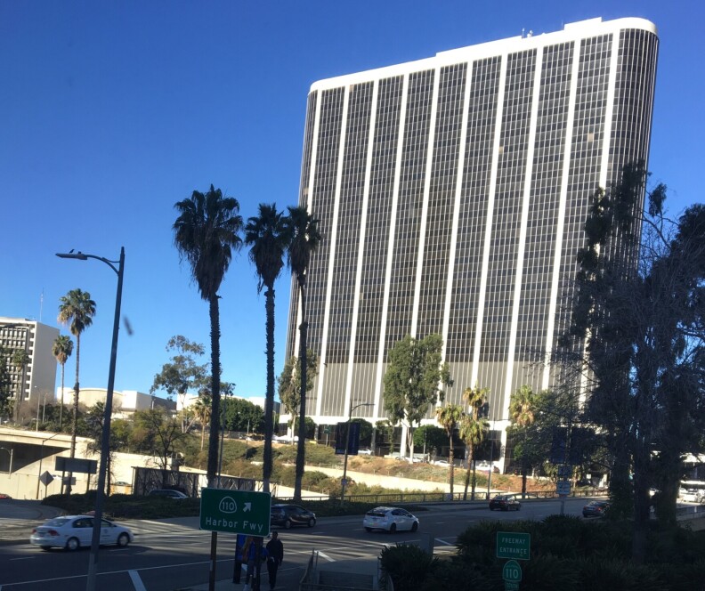 A large office building with palm trees in the foreground near a busy street.
