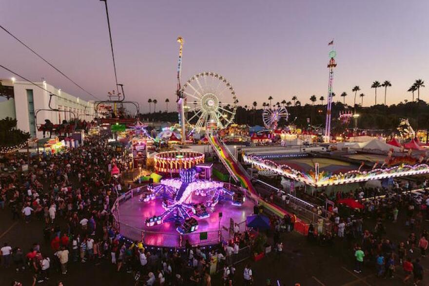 Thousands of people walk through around attractions such as a Ferris wheel, a merry-go-round and other rides at night.