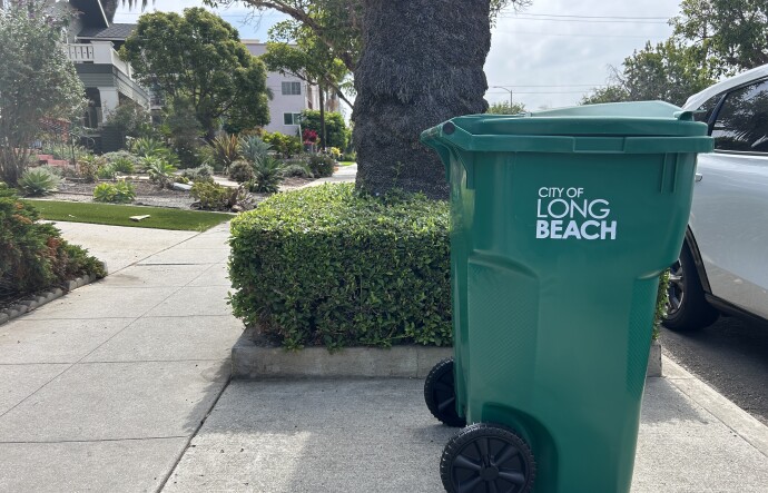 A new green waste bin reads "city of Long Beach" and sits on a sunny sidewalk in an residential neighborhood. 