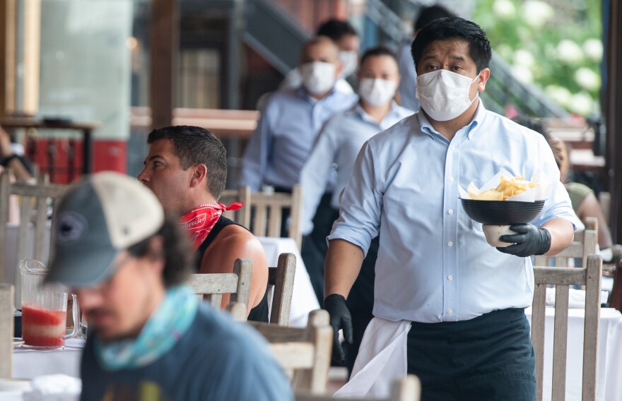 A waiter wearing a mask and gloves delivers food to a table to customers seated at an outdoor patio at a Mexican restaurant in Washington, DC, May 29, 2020. - Friday marks the beginning of phase one in the city with restaurants reopening following the stay at home orders from the COVID-19 pandemic, provided they can serve customers outdoors with groups sitting at least 6 feet apart. (Photo by SAUL LOEB / AFP) (Photo by SAUL LOEB/AFP via Getty Images)