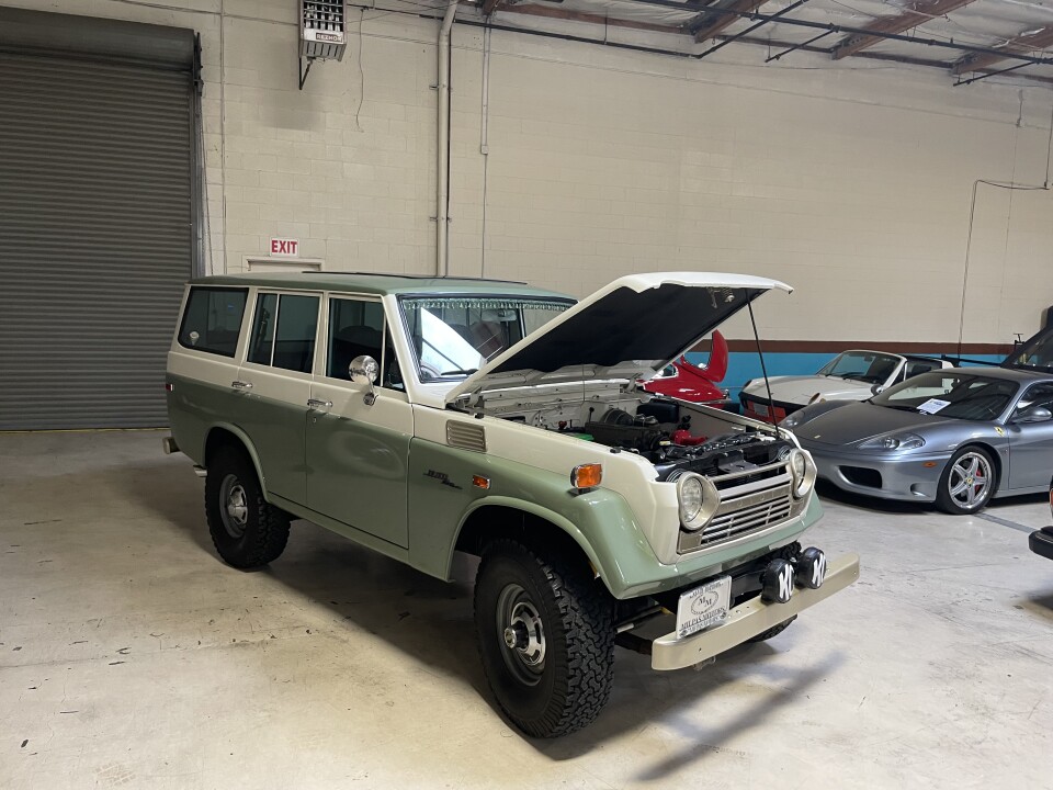 A green and cream jeep with the hood propped open.
