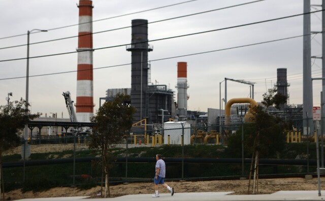 A man walks on a sidewalk in front of large smokestacks.