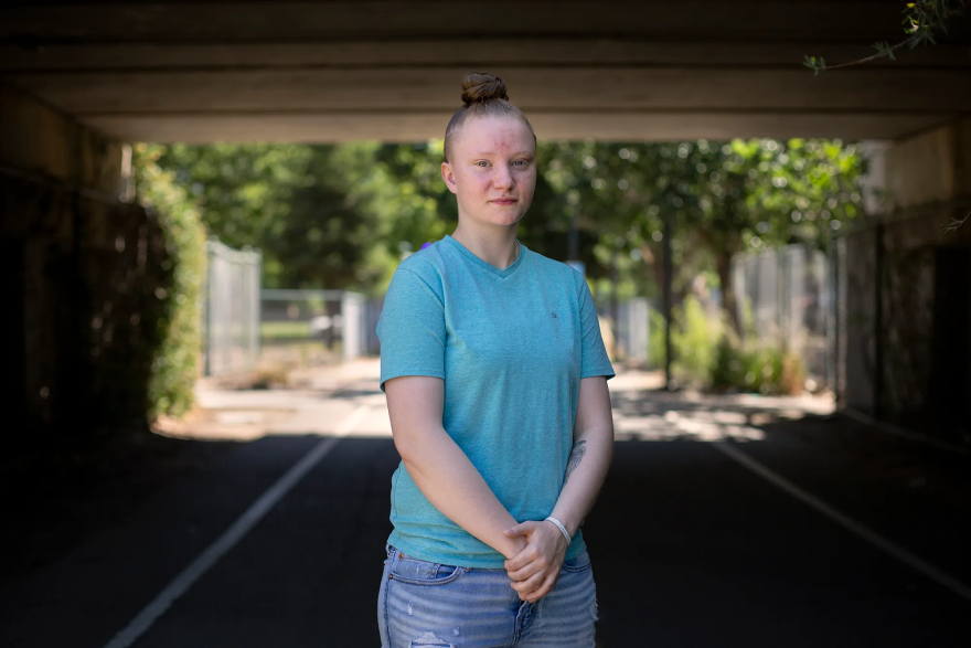 A young woman stands on a shaded path, posing for a photo.