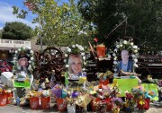 A close-up look at the makeshift memorial outside Cook's Corner, site of a mass shooting that killed three: Home Depot buckets are overflowing with bouquets of flowers. There are flags, signs, notes and three large photos of the victims who died. 