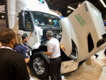 People gather around a large, white electric semi-truck that has it's hood open. 