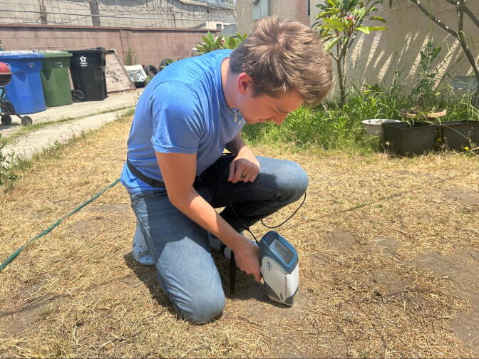 A man uses a tool to scan the grass outside a home.