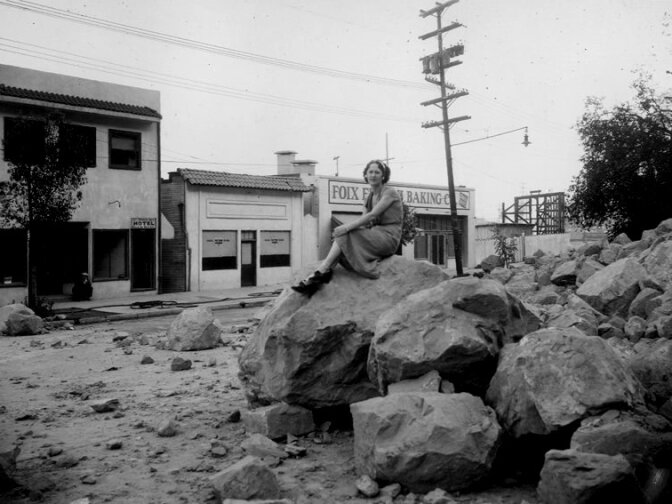 From Nov. 9, 1937: "Elysian Park Landslide on Riverside Drive, looking east from Arnold Street, showing large boulders in roadway, girl sitting on top of boulder. Foix French Baking Co."

