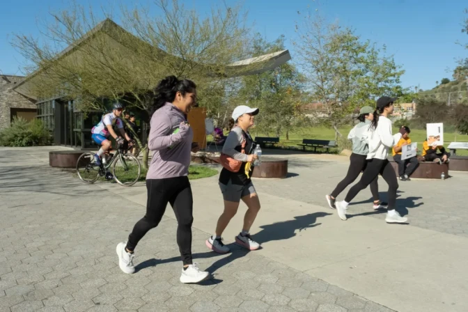 A small group of people run through a park on pavement.