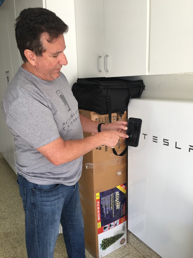 Kirk Nason shows how he tracks the electricity generated by his solar panels on his phone. Some of the power is stored in his Tesla PowerWall, a home battery system visible in the background.