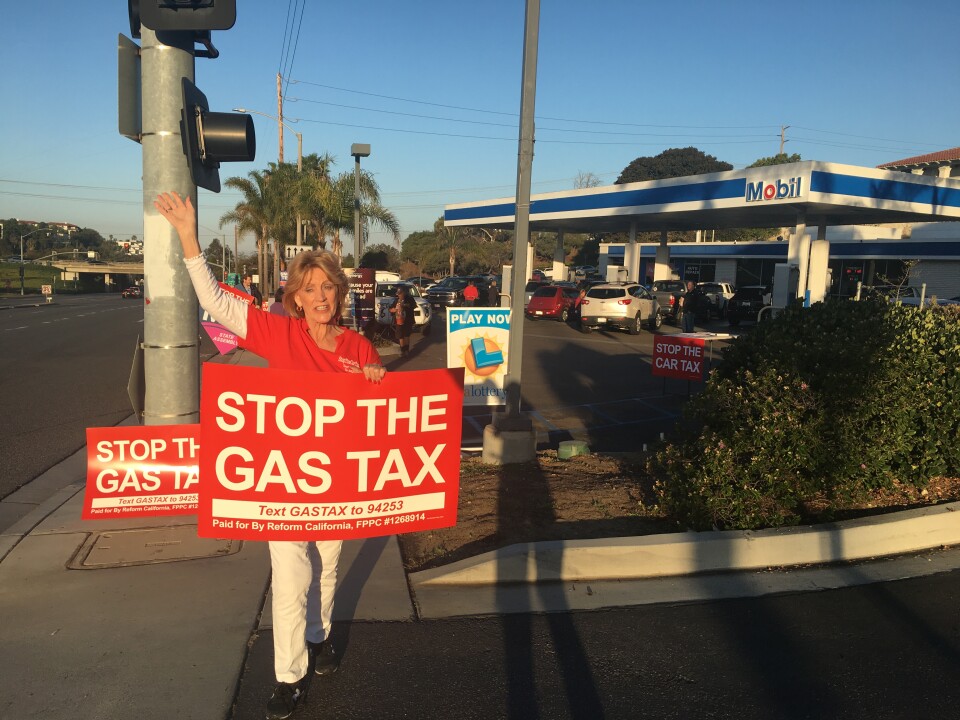 Judy Rees signals drivers into a Mobil gas station near I-5 in Encinitas to get them to sign a petition to repeal the state's new gas tax.