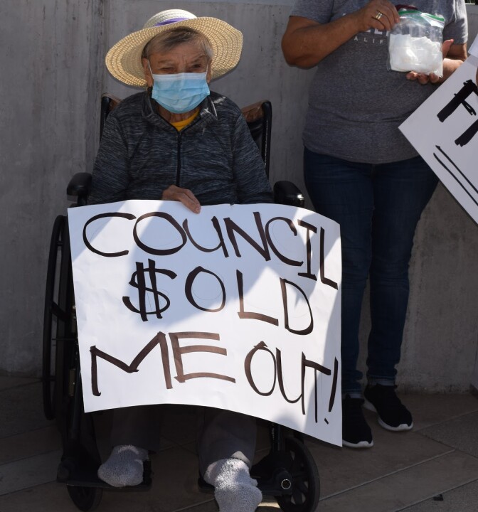 Older woman holds a protest sign saying "council sold me out"
