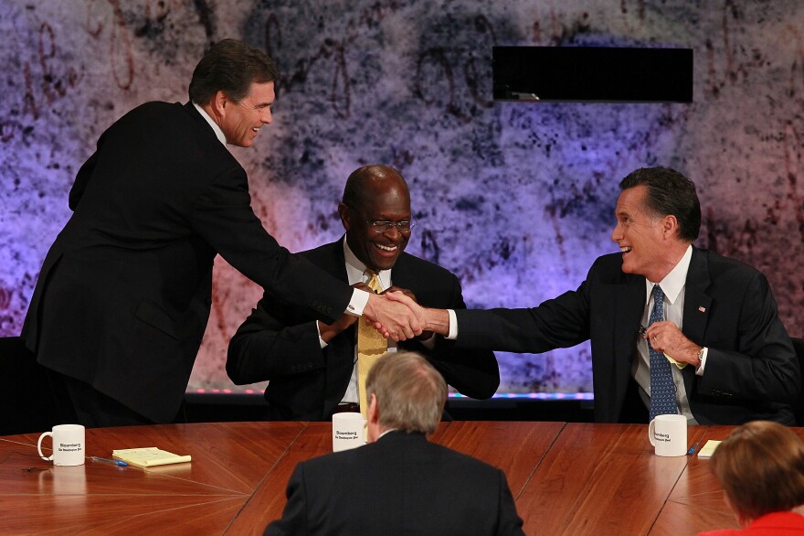 HANOVER, NH - OCTOBER 11:  Former CEO of Godfather's Pizza Herman Cain (C) looks on as Texas Gov. Rick Perry (L) and Former Massachusetts Gov. Mitt Romney shake hands.

<br><br>On October 18, Community Advocates Inc. will honor Larry Mantle with the Bill Stout Memorial Award for Excellence in Broadcast Journalism. To attend, RSVP to cai@cai-la.org or call (213) 623-6003 ext. 10.