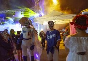 A view of two people in crowd outside at night. They have their faces painted to look like skulls and they're wearing blue dodgers memorabilia. One person on the left is wearing a nun headpiece. In the background are blue and yellow lights radiating through the fog.