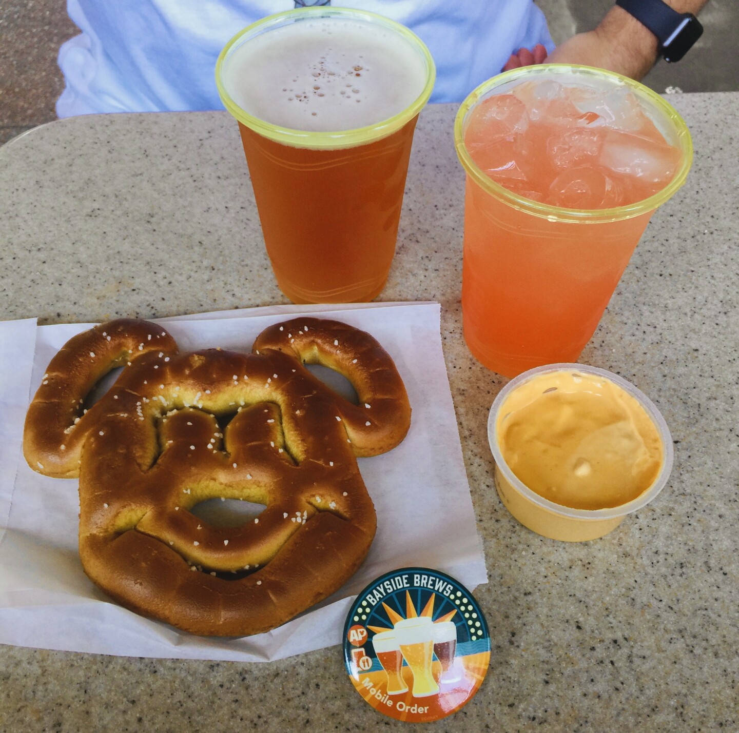 A pretzel shaped like Mickey Mouse sits next to a small container of orange nacho cheese.