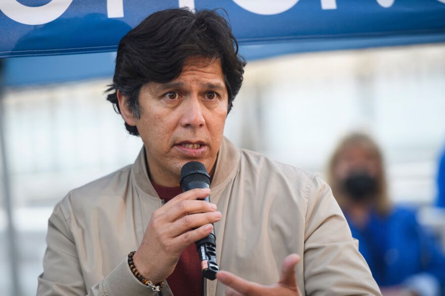 L.A. City Councilmember Kevin de León wears a tan jacket and speaks into a microphone at an event in Redondo Beach.