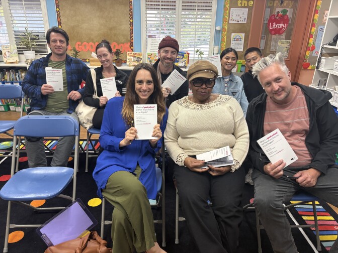 Multiple parents are sitting in chairs in a classroom, holding LAist's workbooks titled "What is a 'good school' and how do you find one in Los Angeles?"