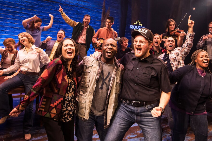 A crowd of people on a theater stage singing together.