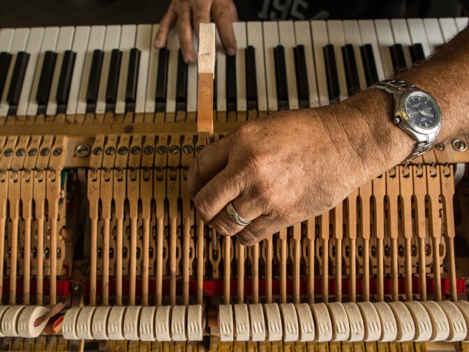 Enrique Beruman, a piano repair technician, tests the action on a piano keyboard.