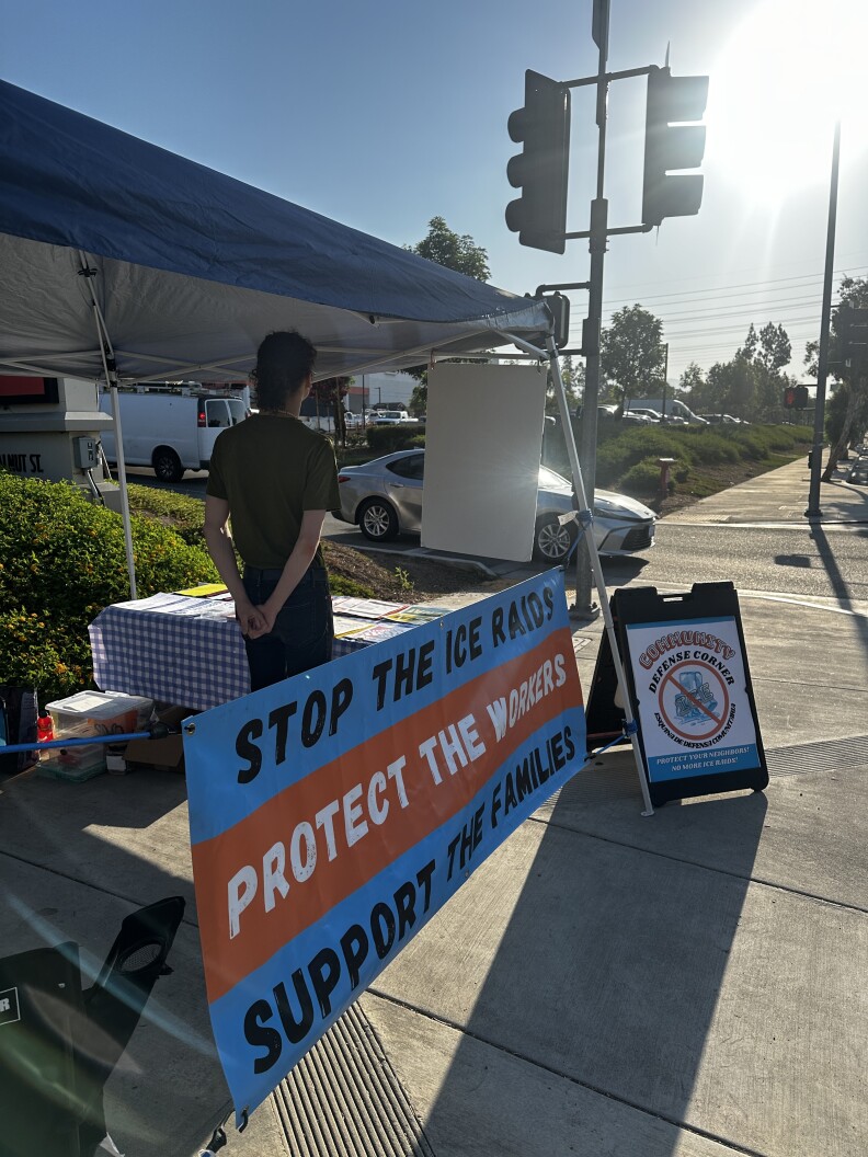 A volunteer is seen standing at the East Pasadena Community Defense Corner table.