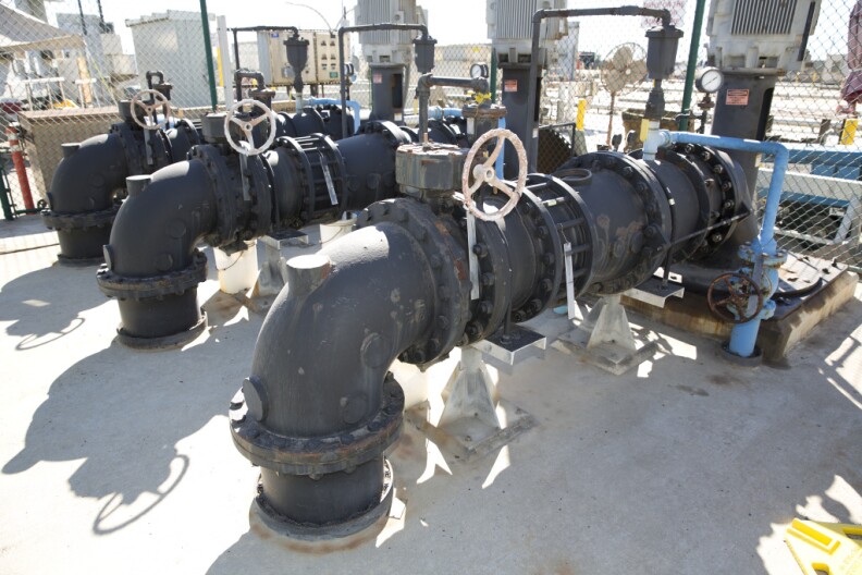 Three very large pipes rise from a concrete floor and make a right-angle to another part of a water treatment plant
