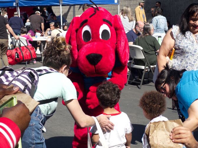 a person in a bright red dog costume approaches some kids